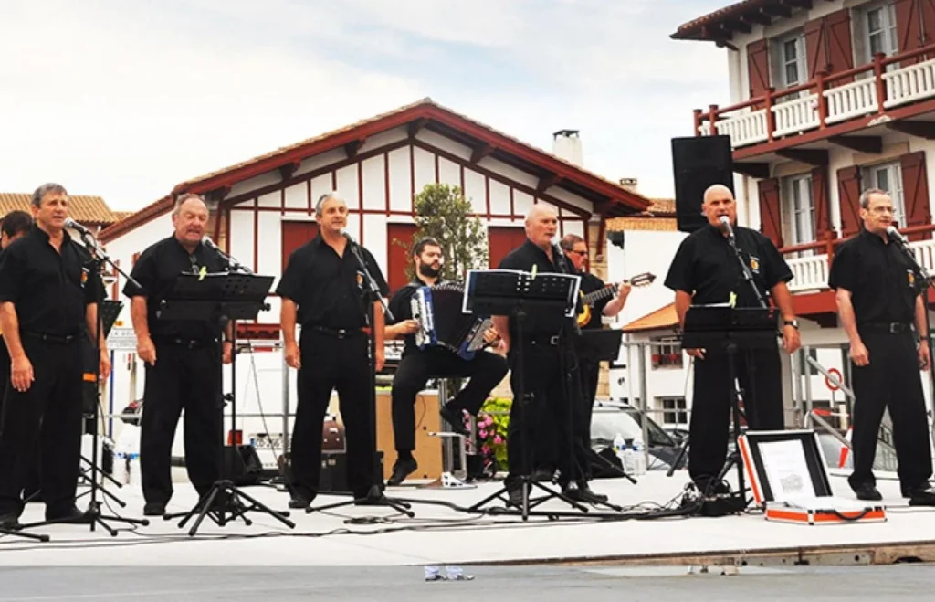 Groupe de chanteurs basques en concert en plein air à Urrugne, interprétant des chants traditionnels.