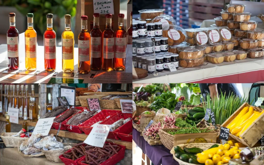 Produits locaux exposés au marché de Saint-Jean-Pied-de-Port, avec des bouteilles artisanales, des biscuits, des saucissons et des légumes frais.