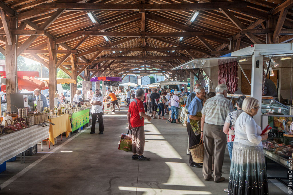 Vue intérieure des halles du marché de Saint-Jean-Pied-de-Port, avec des stands de produits locaux et des visiteurs découvrant des spécialités basques.