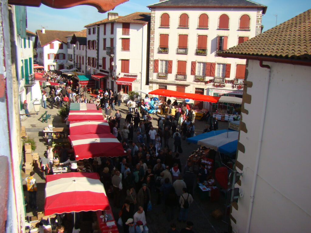 Vue animée du marché d'Espelette, avec des stands colorés et des visiteurs découvrant des produits locaux au cœur du Pays Basque