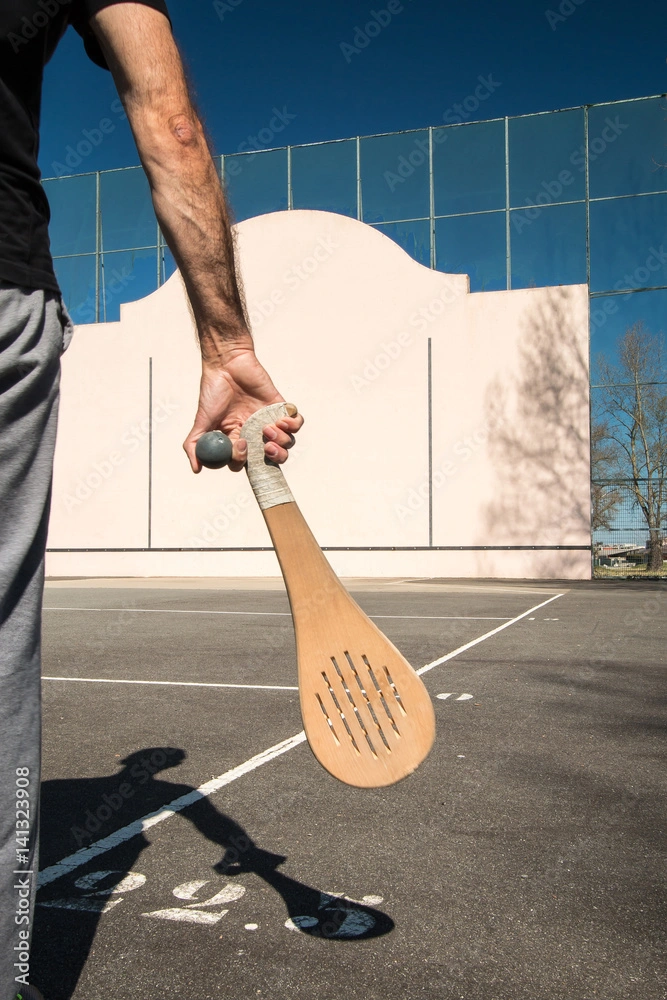 Joueur tenant une pala en bois devant un fronton basque en plein air.