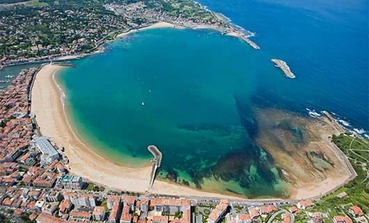 Vue panoramique d'une plage de la côte basque avec l'océan Atlantique, le sable et les montagnes en arrière-plan.